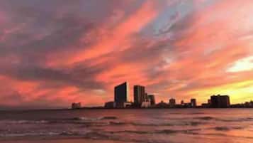Stunning coastal city skyline with modern high-rise buildings and a unique skyscraper overlooking the calm sea.