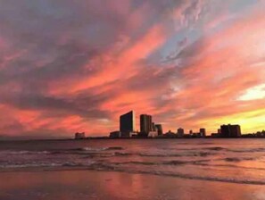 Paisagem urbana costeira ao pôr do sol, com prédios em silhueta contra um céu colorido.