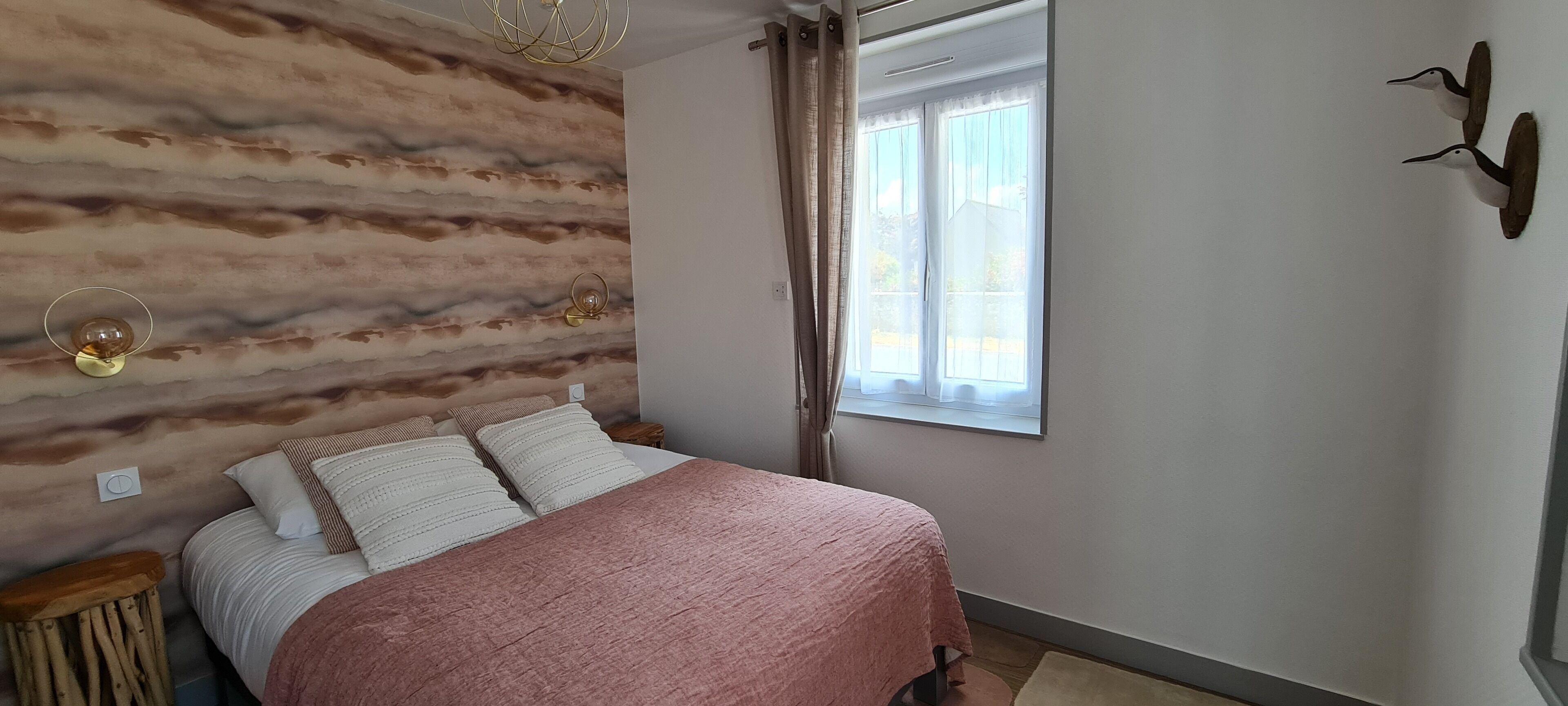 Een slaapkamer met een bed, een raam, een wandlamp en een decoratieve vogel aan de muur.