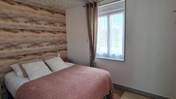 Een slaapkamer met een bed, een raam, een wandlamp en een decoratieve vogel aan de muur.