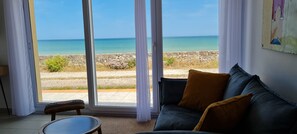 A room with a view of the sea, a sofa with cushions, a small table, and a curtain. - Gite la mer, les pieds dans l'eau for 4 people (Saint-Marcouf)
