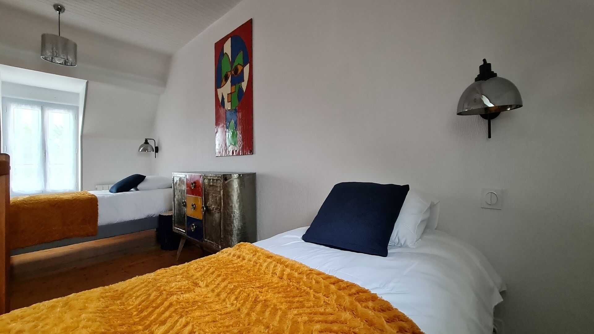 A hotel room with two beds, a colorful abstract painting, a lamp, and a wardrobe.