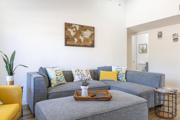 A modern living room with a grey sectional sofa, a small coffee table with a tray, and a potted plant.