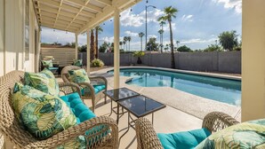 A covered patio with wicker furniture, a glass table, and a swimming pool. - 4-min to Kierland- Heated Pool & Outdoor Dining, Scottsdale Gem (Scottsdale)