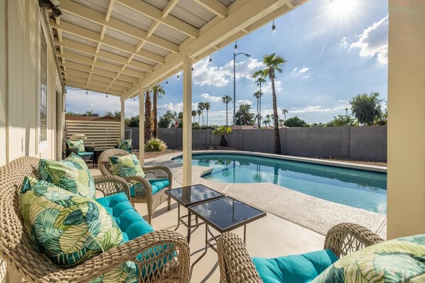 Une terrasse couverte, aménagée avec des meubles en osier, une table en verre et une piscine.