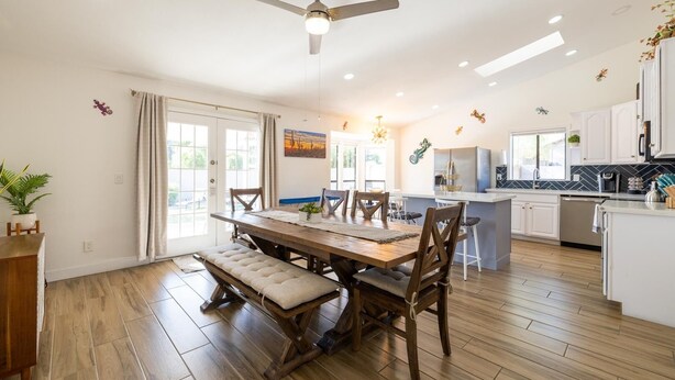 A modern kitchen with white cabinets, a central island, and a dining area with a wooden table and chairs. - 4-min to Kierland- Heated Pool & Outdoor Dining, Scottsdale Gem (Scottsdale)