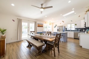 Une cuisine moderne avec des meubles blancs, un îlot central et un coin repas comprenant une table et des chaises en bois.