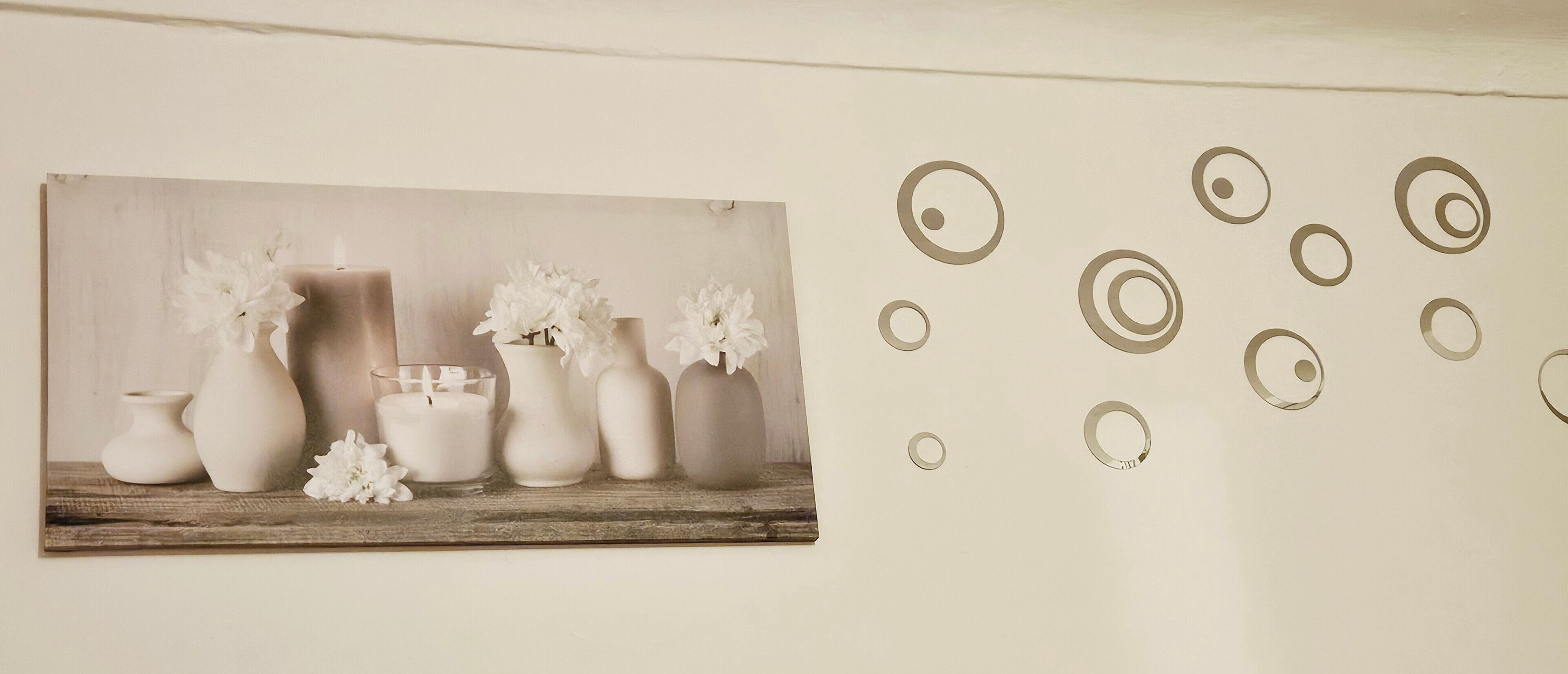Una pared con un marco que contiene una fotografía de jarrones y flores, y un adhesivo mural con círculos concéntricos.