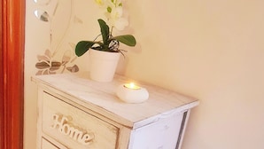 Un meuble d’angle avec des tiroirs étiquetés « Maison », « Vie » et « Amour ». Une plante en pot et une bougie sont posées sur le dessus.