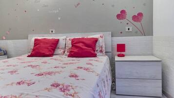 Une chambre à coucher avec un lit, deux oreillers, une table de chevet et un mur décoré de motifs en forme de cœur.