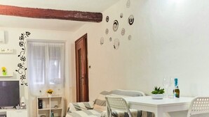 Un salon confortable avec un canapé, une table à manger et des chaises, un téléviseur et une fenêtre avec des rideaux.