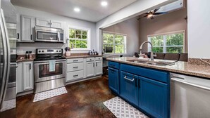 A modern kitchen with stainless steel appliances, blue cabinets, and a window overlooking greenery.