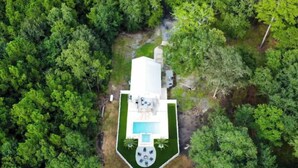 An aerial view of a modern house with a swimming pool, surrounded by dense greenery.