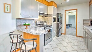 Una cocina con encimeras de granito, electrodomésticos de acero inoxidable, armarios de madera y una isla integrada con taburetes de bar.