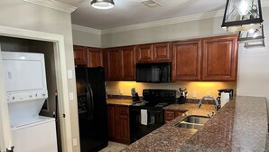 A kitchen with wooden cabinets, a black refrigerator, a microwave, a stove, and granite countertops.