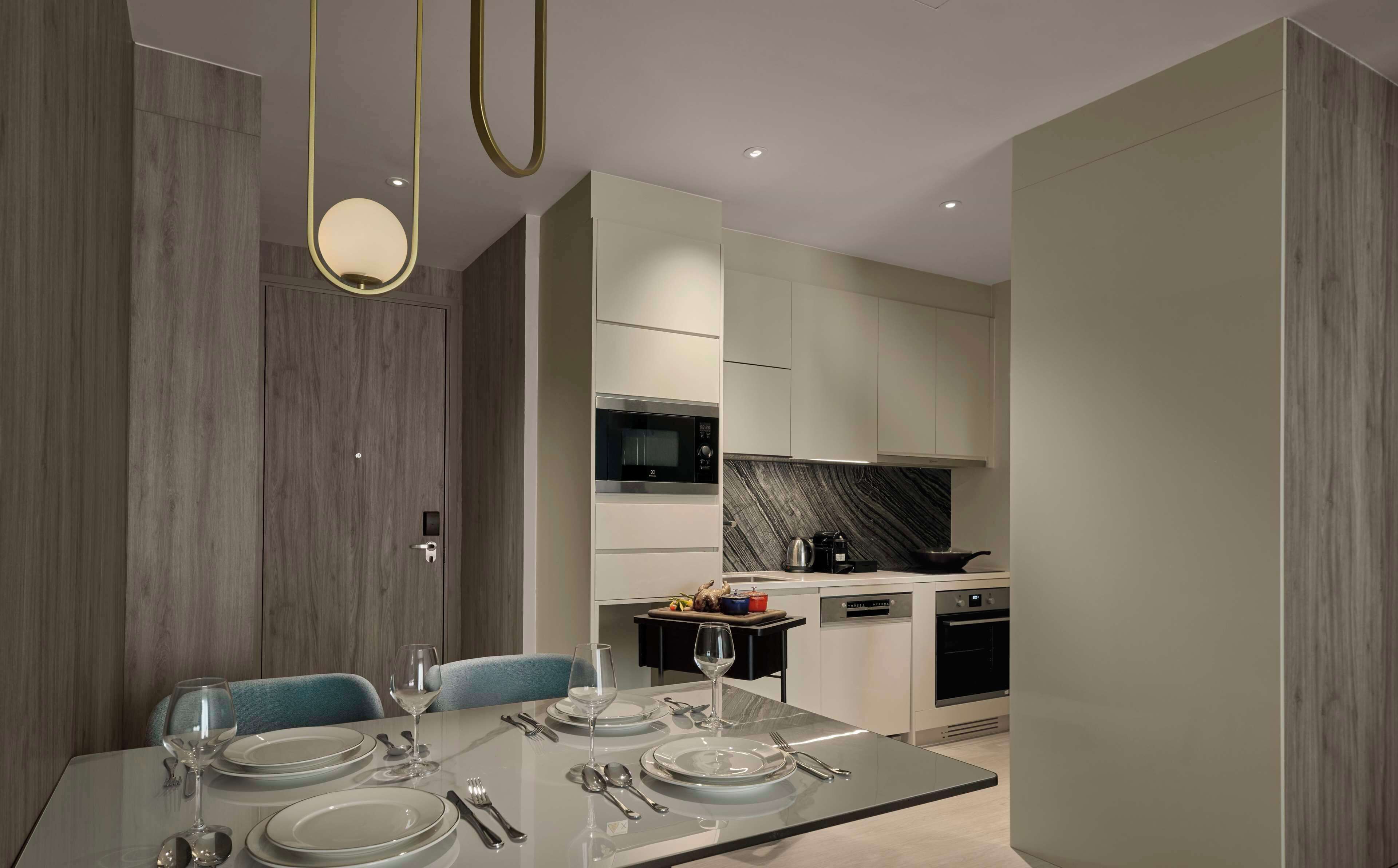 A modern dining area with a glass table, chairs, and a kitchen in the background.