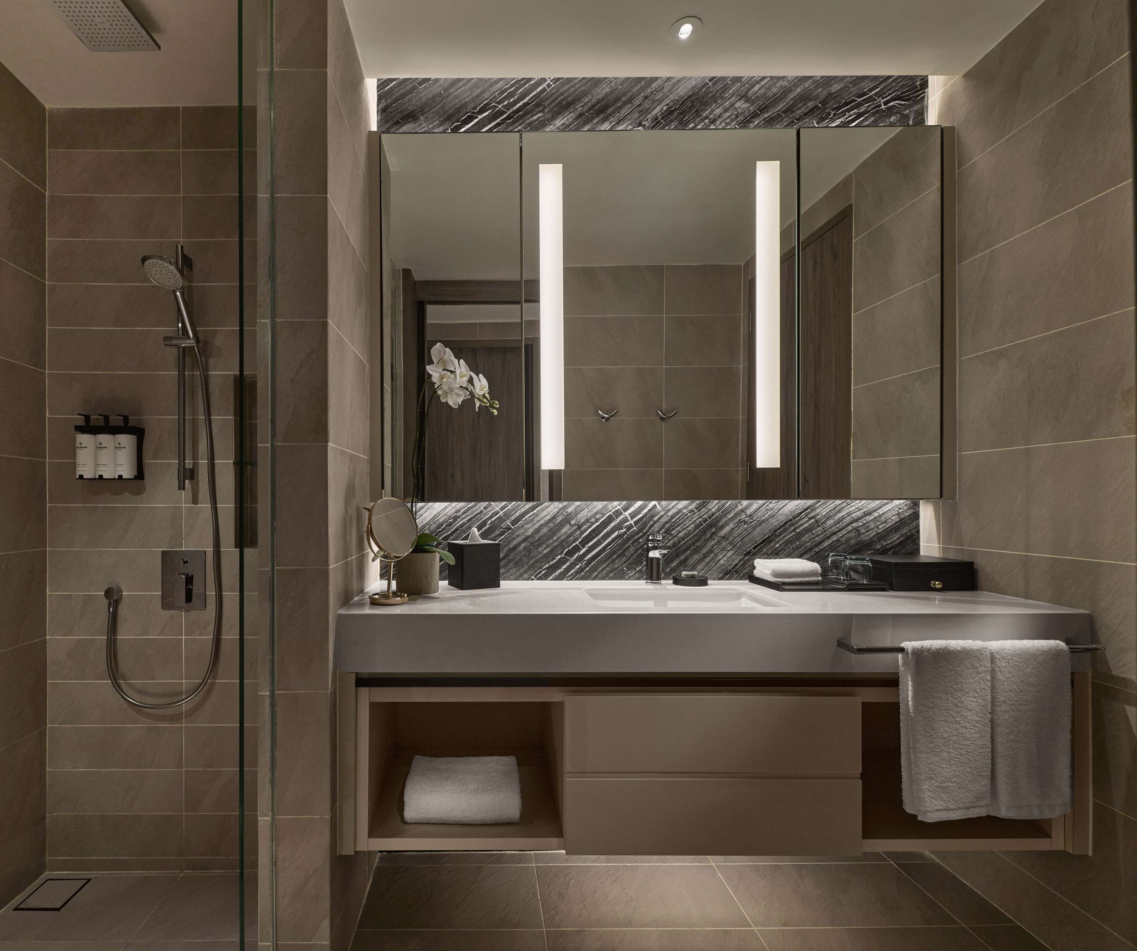 A modern bathroom with a large mirror, a shower, and a vanity with a towel rack.