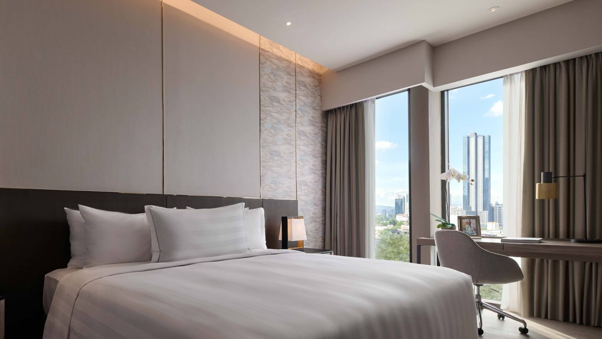 A modern hotel room with a large bed, a desk, and a city view.