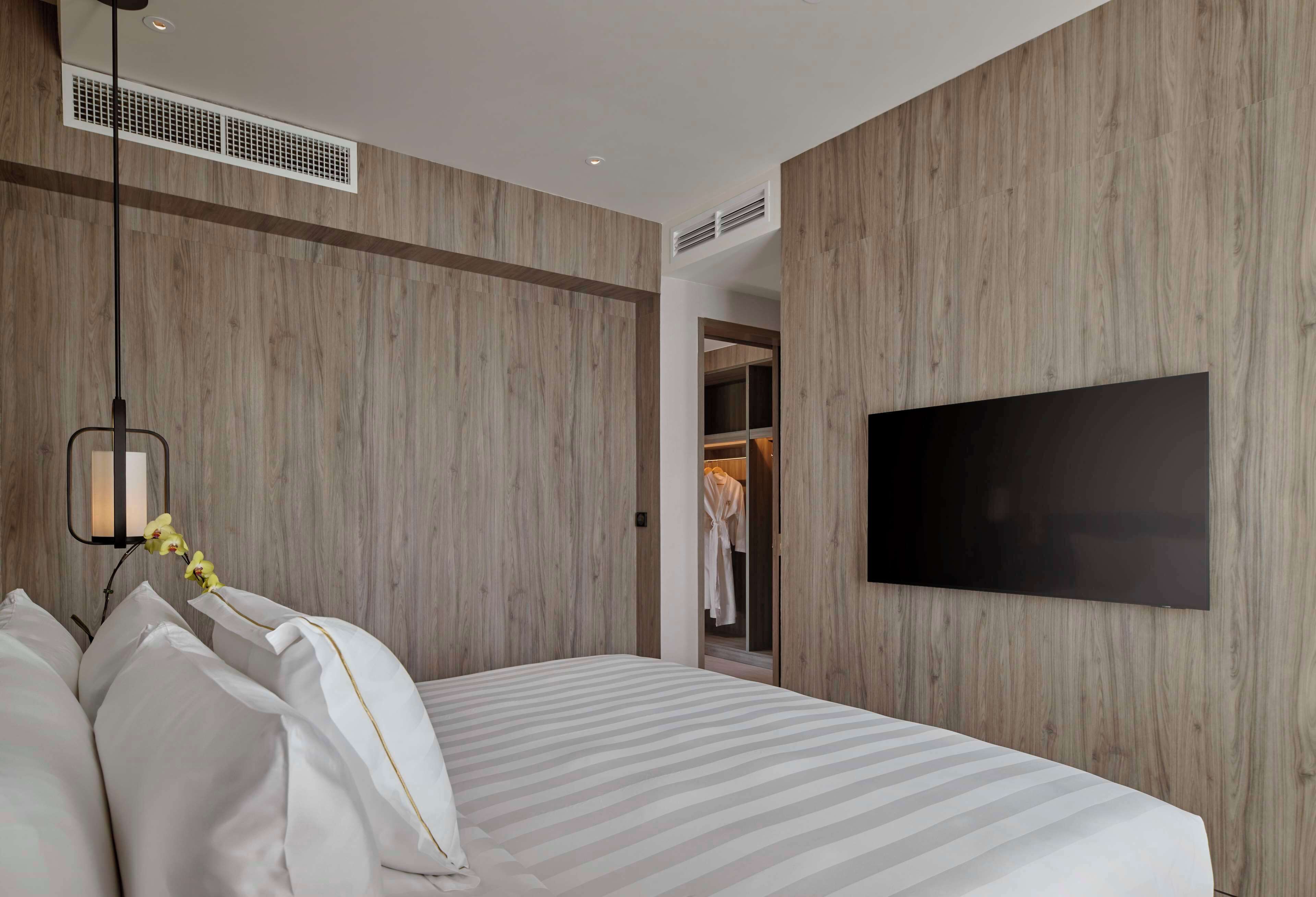 A modern bedroom with a large bed, a mounted TV, and a walk-in closet.