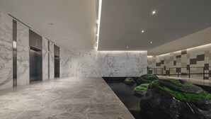 Een moderne lobby met marmeren wanden, liften, een fontein met rotsen en een wand met een geometrisch patroon.
