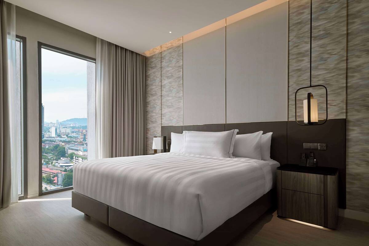 Une chambre d’hôtel moderne avec un grand lit, une table de chevet, une lampe et une vue sur la ville.