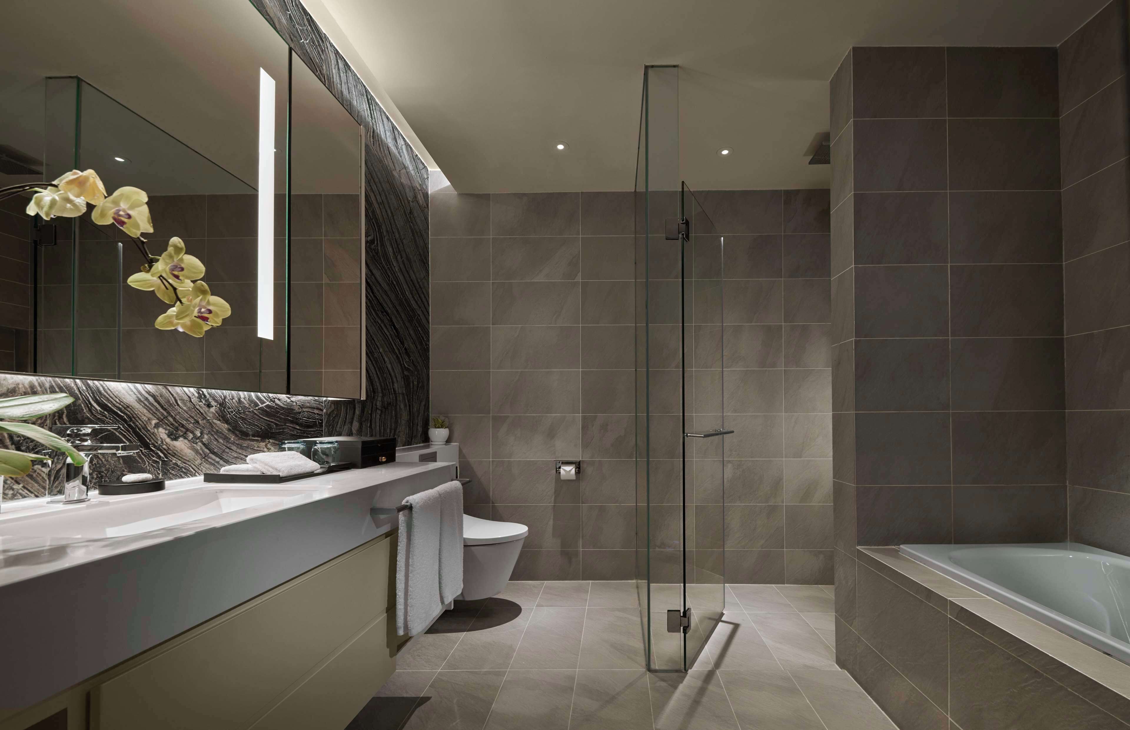 Un baño moderno con ducha envuelta en vidrio, bañera y tocador de mármol.