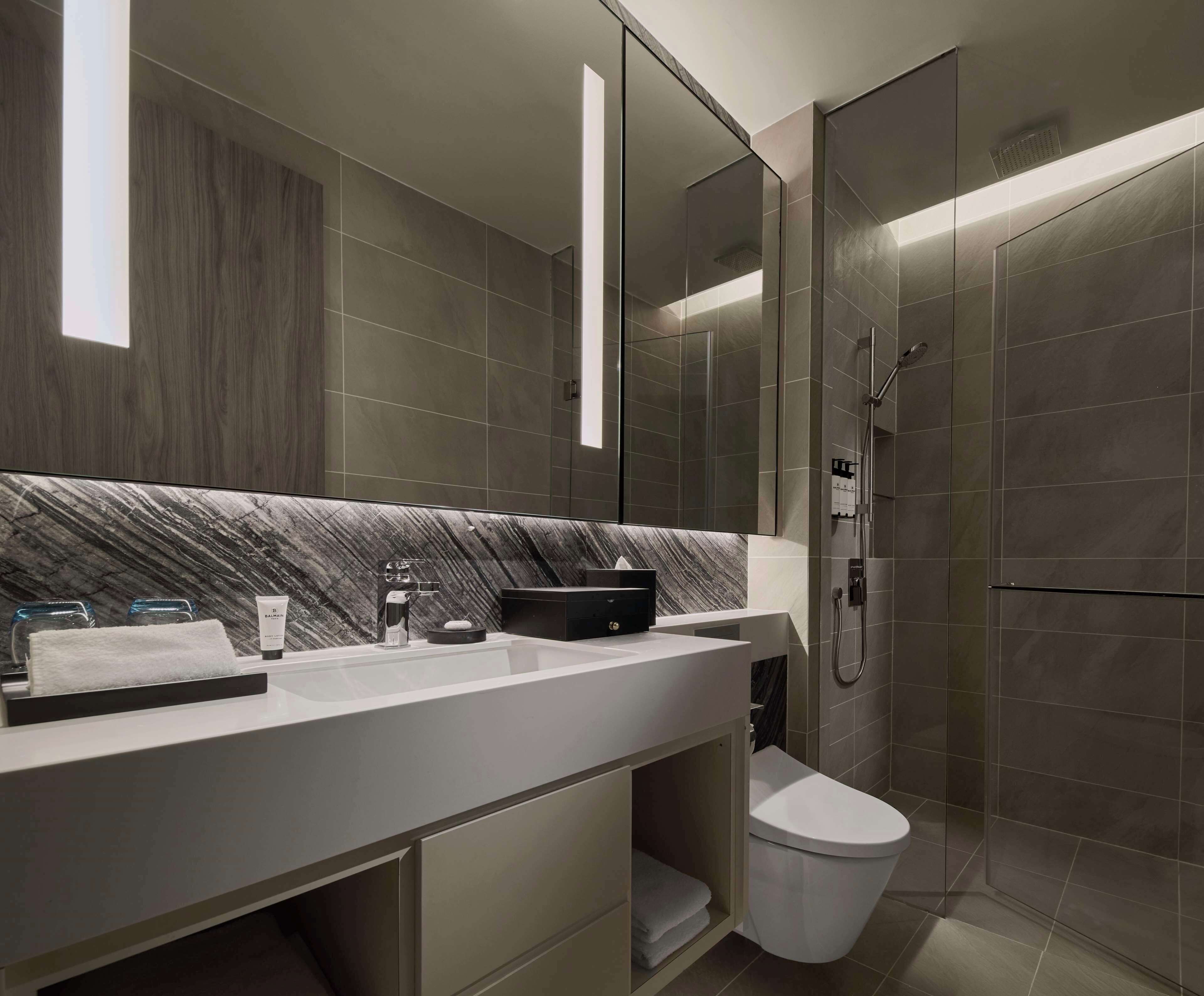 A modern bathroom with a marble backsplash, a white sink, a toilet, and a glass-enclosed shower.