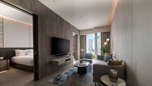 Een moderne hotelkamer met een bed, een flatscreen televisie, een bank, een salontafel en uitzicht op de stad.