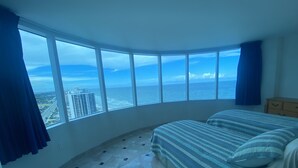 Een slaapkamer met een gebogen raam, met uitzicht op de oceaan en verre gebouwen.
