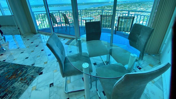 Een balkon met een glazen tafel en stoelen, met uitzicht op een stadsgezicht en water.