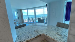 Een ruime kamer met een groot raam en uitzicht op zee, plus een balkon met stoelen.