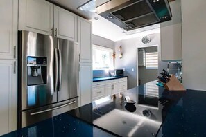 Cozinha moderna com eletrodomésticos de aço inoxidável, bancada preta e janela que permite entrada de luz natural.