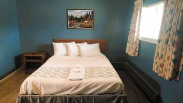 A neatly made bed with a headboard, a bedside table, and a painting of a mountain landscape on the wall.