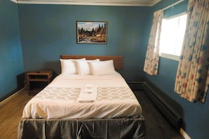 A neatly made bed with a headboard, a bedside table, and a painting of a mountain landscape on the wall. - Love Hotels Desert Inn & RV at Boysen Wind River (Shoshoni)