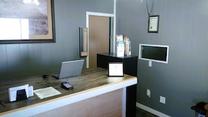 A reception desk with a laptop, a phone, and a computer monitor. There is a framed certificate on the wall and a trash can to the right. - Love Hotels Desert Inn & RV at Boysen Wind River (Shoshoni)