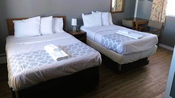 A hotel room with two beds, each with a pillow and a bedside table with a lamp.