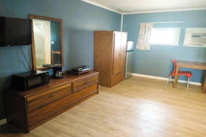 A room with a wooden dresser, a flat-screen TV mounted on the wall, a wooden cabinet, a red chair, and a window with a curtain. - Love Hotels Desert Inn & RV at Boysen Wind River (Shoshoni)