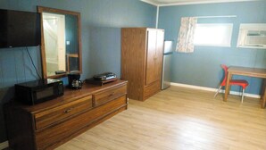 A room with a wooden dresser, a flat-screen TV mounted on the wall, a wooden cabinet, a red chair, and a window with a curtain. - Love Hotels Desert Inn & RV at Boysen Wind River (Shoshoni)