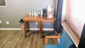 Una habitación pequeña con una mesa de madera, una silla azul y un ventanal con cortina.