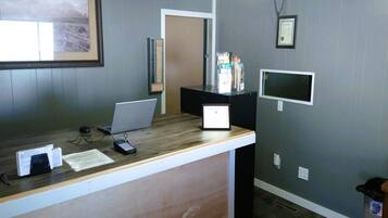 A reception desk with a laptop, a desktop computer, a telephone, and a trash bin.