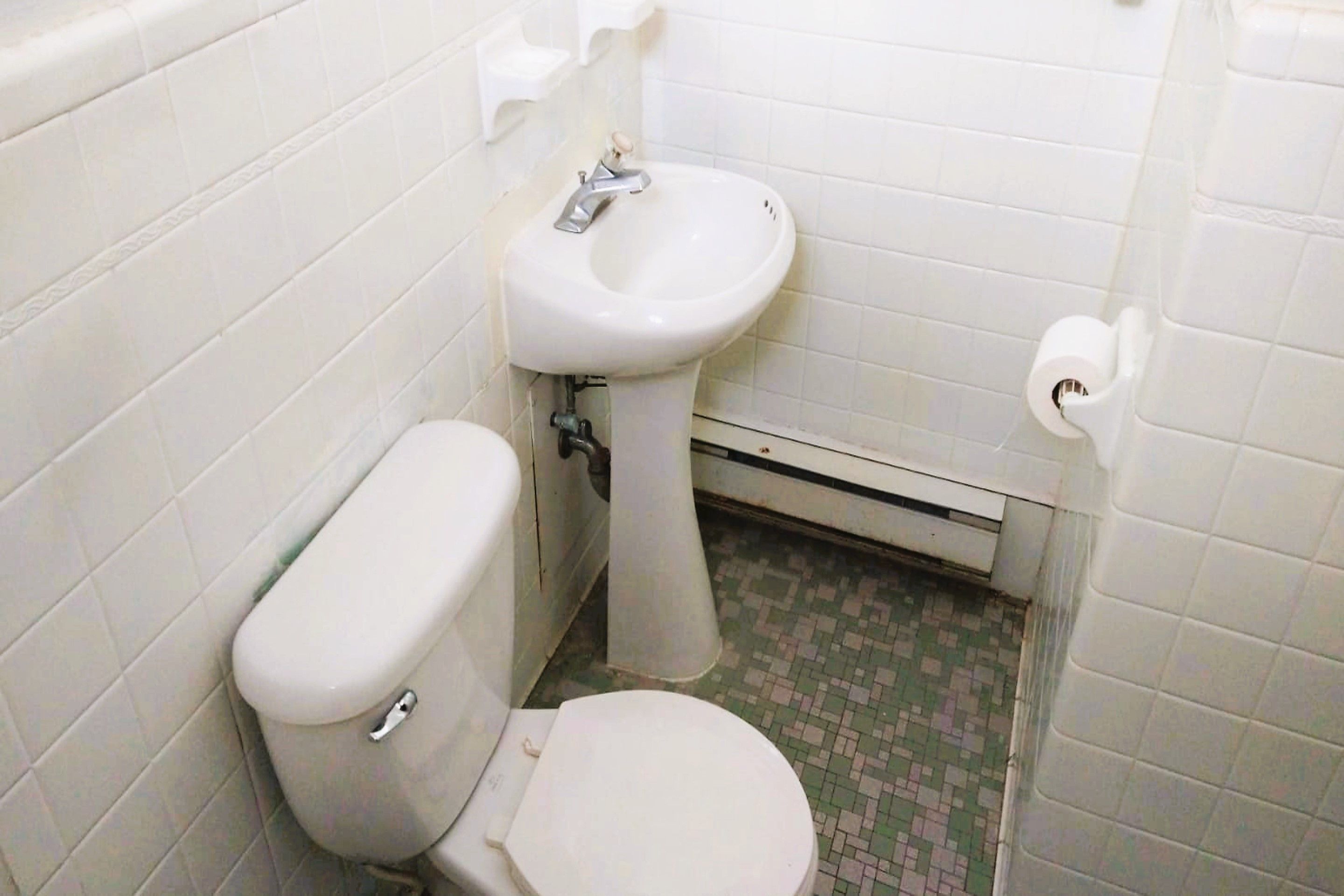 A small, basic bathroom with a toilet, sink, and a toilet paper holder.