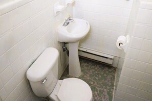 A small, basic bathroom with a toilet, sink, and a toilet paper holder. - Love Hotels Desert Inn & RV at Boysen Wind River (Shoshoni)