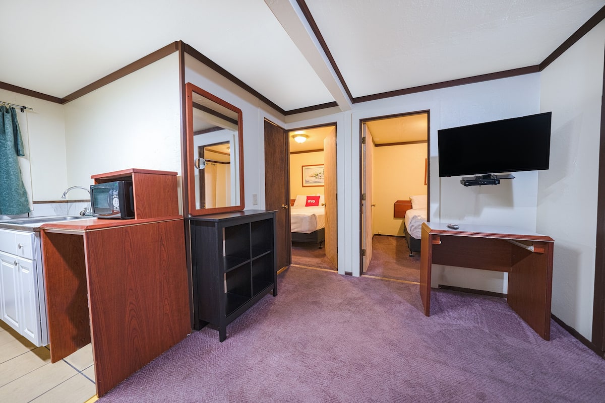 A compact hotel room with a kitchenette, a TV mounted on the wall, and a small desk.