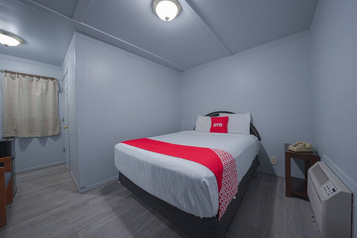 A bedroom with a bed, a bedside table with a phone, and a heater.