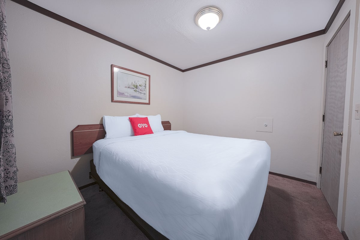 A hotel room with a bed, a nightstand, a framed picture on the wall, and a door.