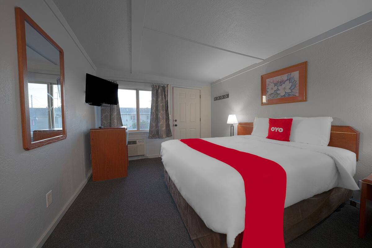 A hotel room with a large bed, a TV, a desk, and a window with curtains.