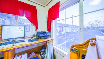 A room with a desk, computer, printer, and a window with a view of a parking lot.