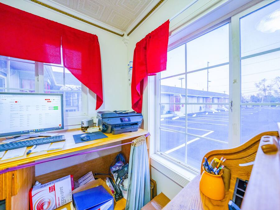 A room with a desk, computer, printer, and a window with a view of a parking lot.