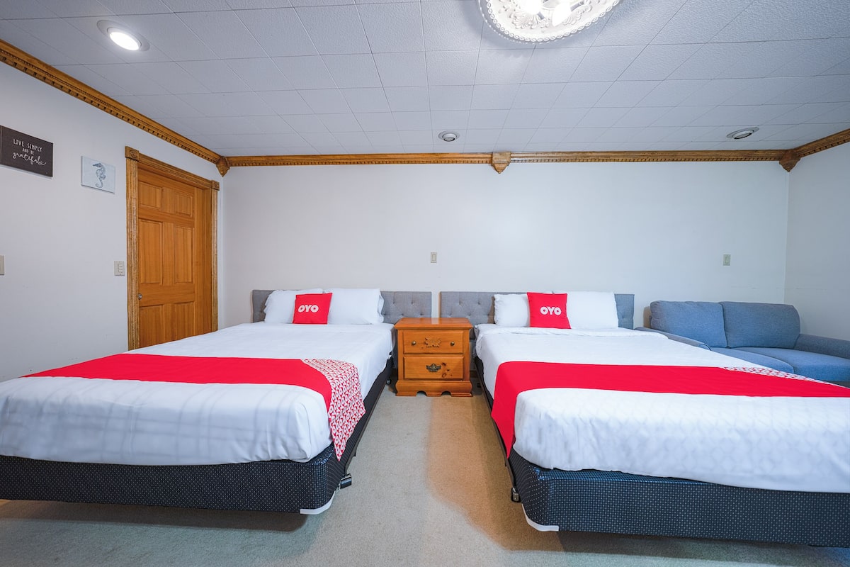 A hotel room with two beds, a wooden nightstand, a blue sofa, and a white ceiling with a circular light fixture.