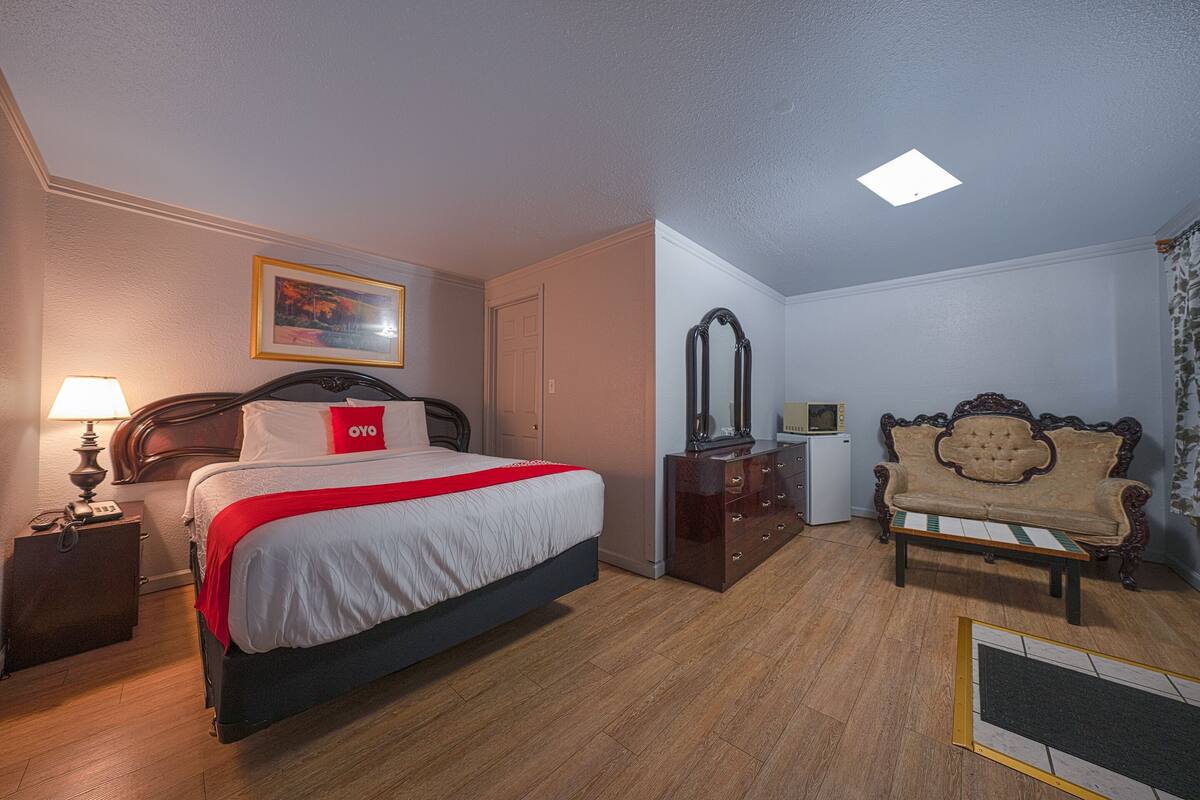 A hotel room with a bed, bedside table, lamp, dresser, mirror, and a vintage sofa.